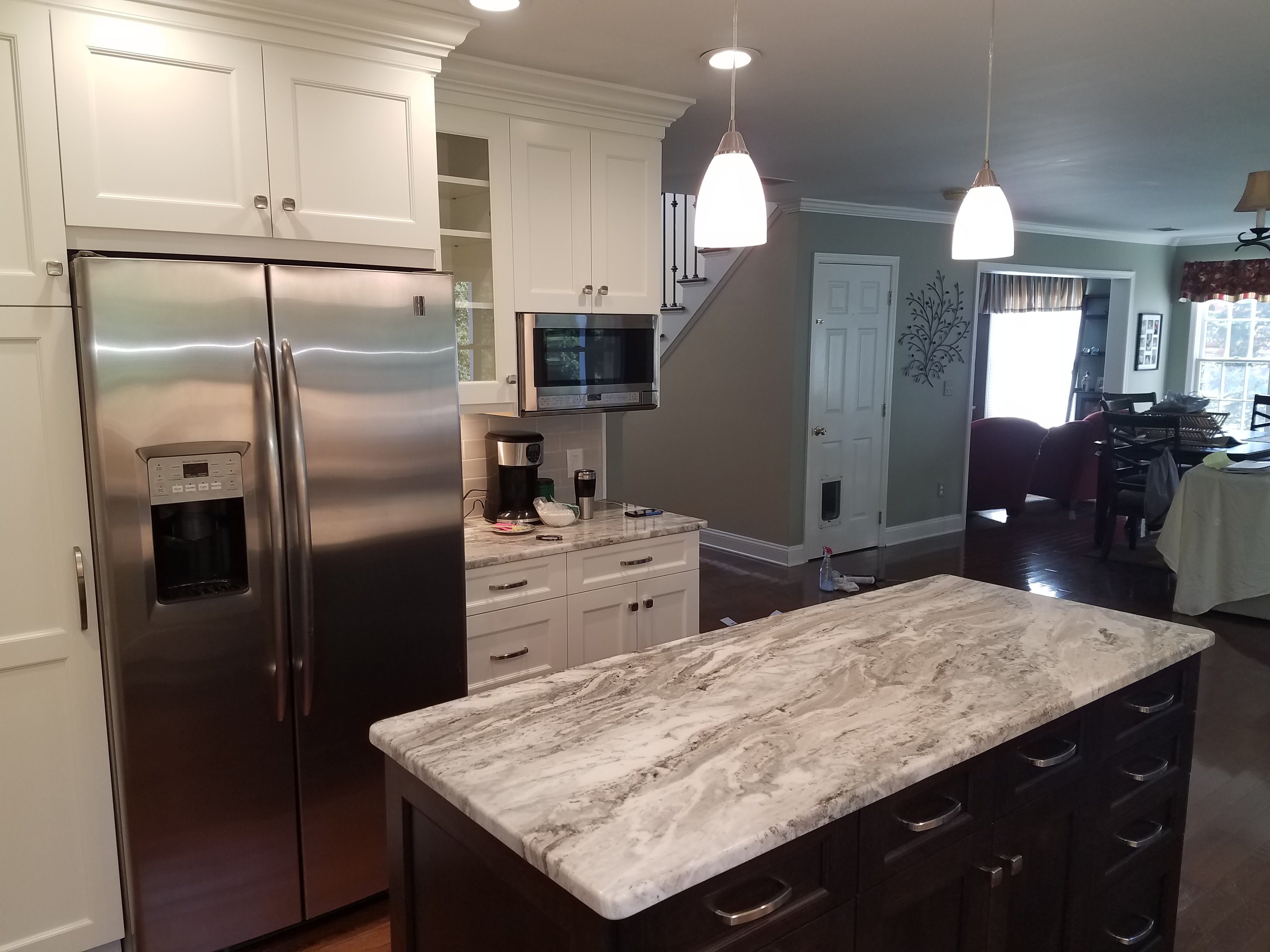 White cabinetry and a stainless steel side-by-side refrigerator open onto a hallway with a staircase and living room.