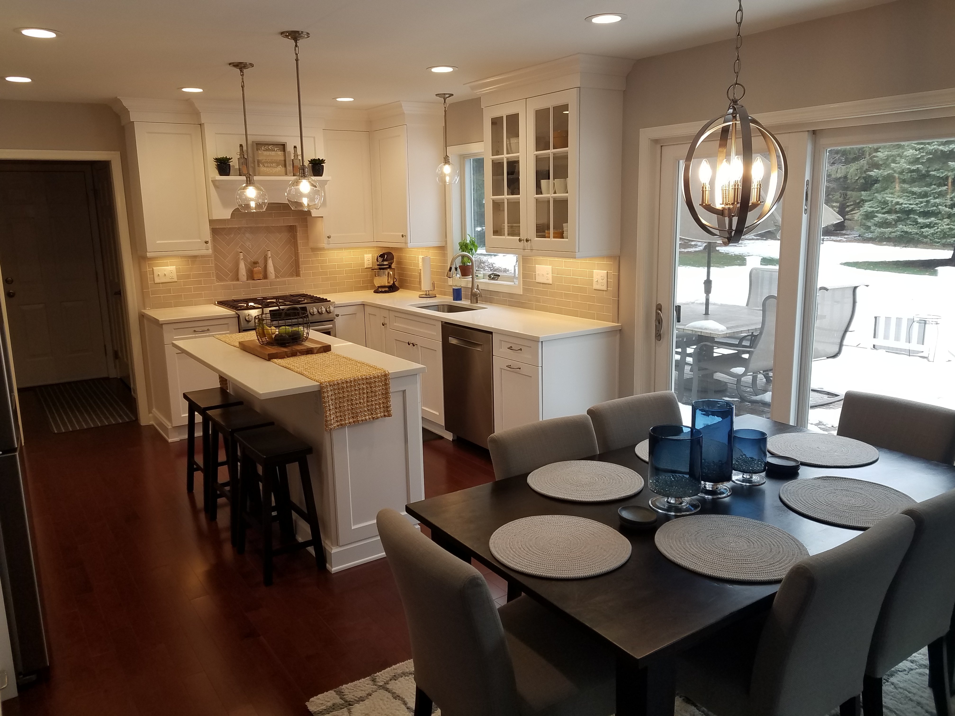 White shaker cabinets and white quartz countertops surround a stainless steel gas range set into a beige herringbone tile backsplash accent.