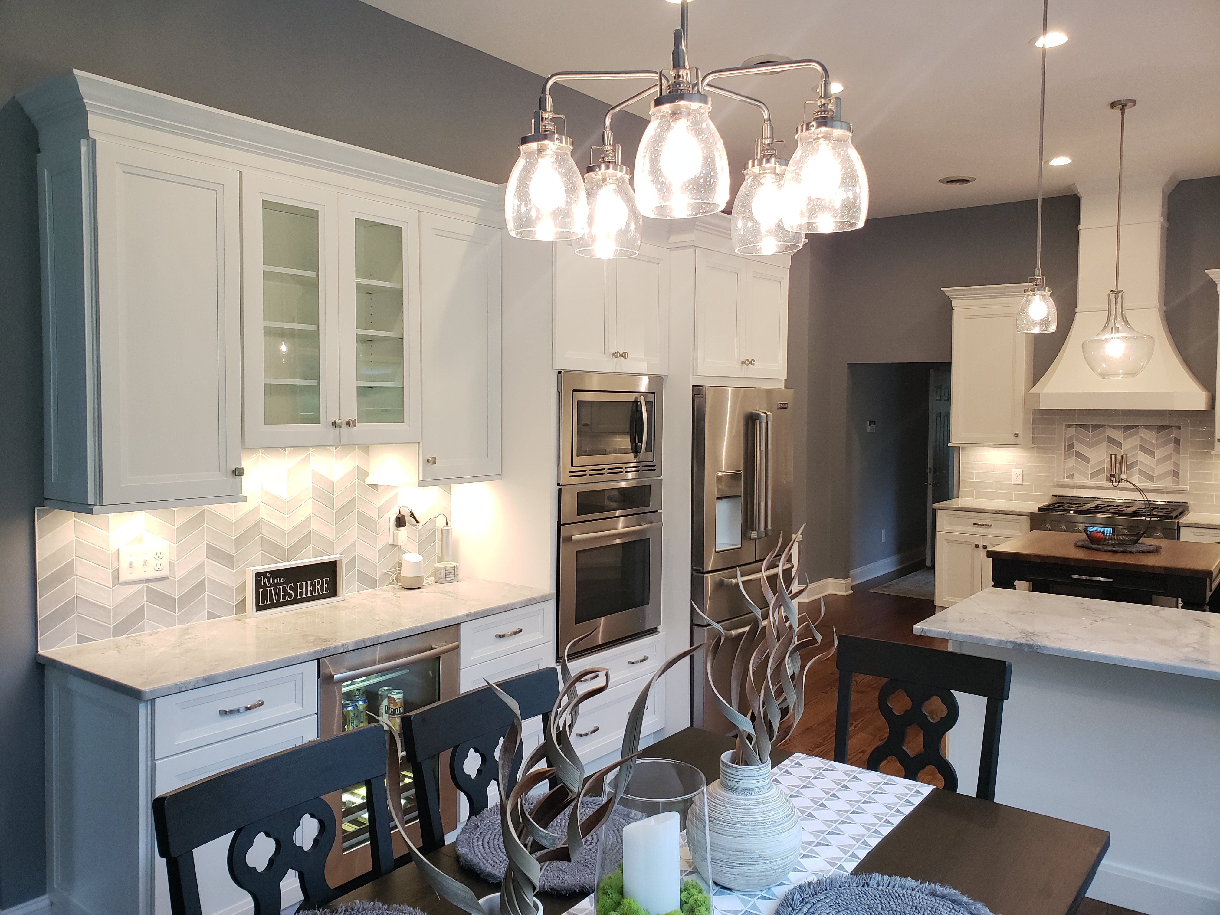 White and pale blue cabinets frame a kitchen with a chevron tile backsplash, marble countertops, and built-in stainless steel oven, microwave, and refrigerator.