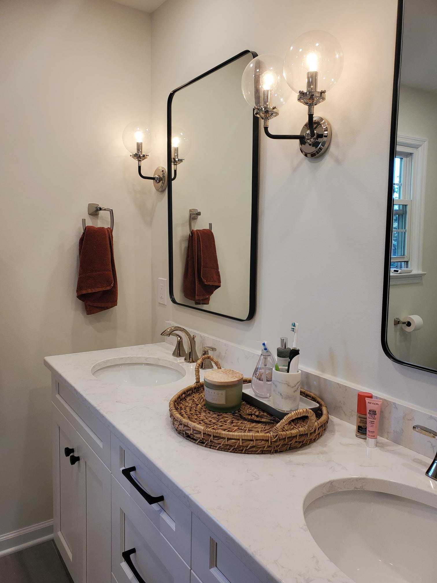 An undermount sink sits beneath a black-framed mirror and polished nickel sconces on a white quartz countertop with subtle gray veining.