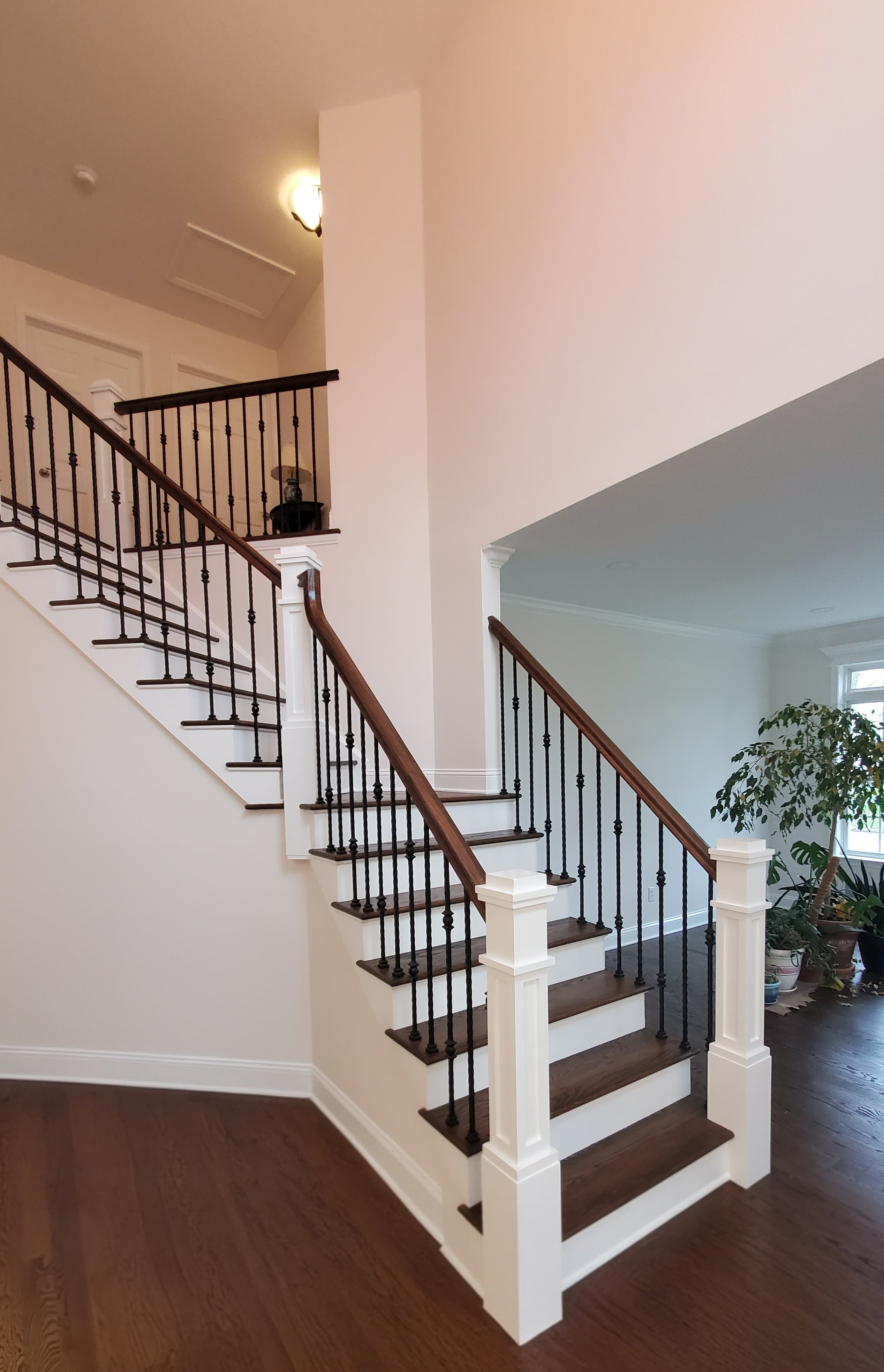 Dark stained wood treads with white risers, a wood handrail, and black wrought-iron balusters descend between white newel posts.