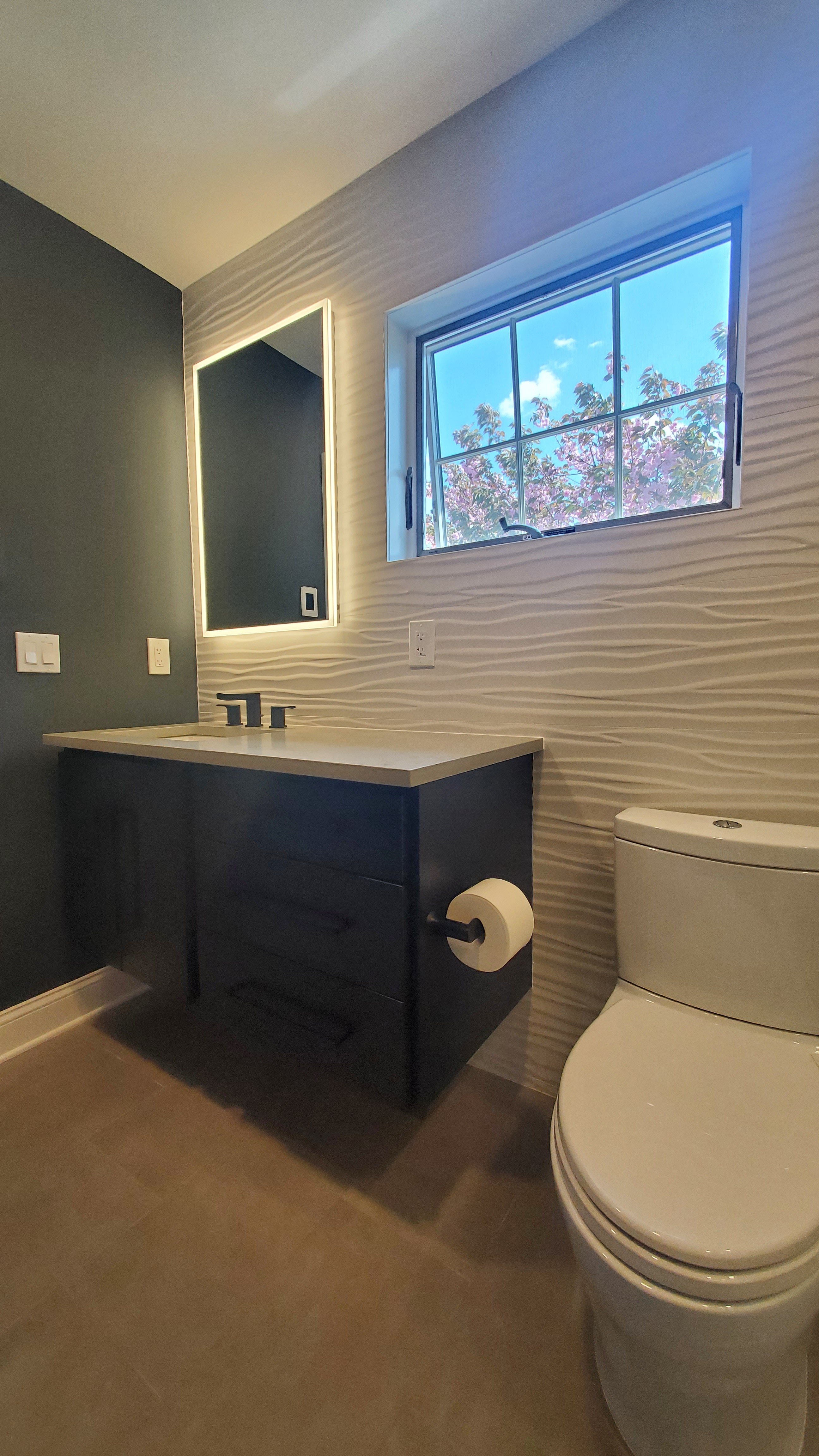 A dark navy floating vanity with a black quartz countertop and matte black wall-mount faucet sits below a black-framed square mirror on a ribbed white wall.