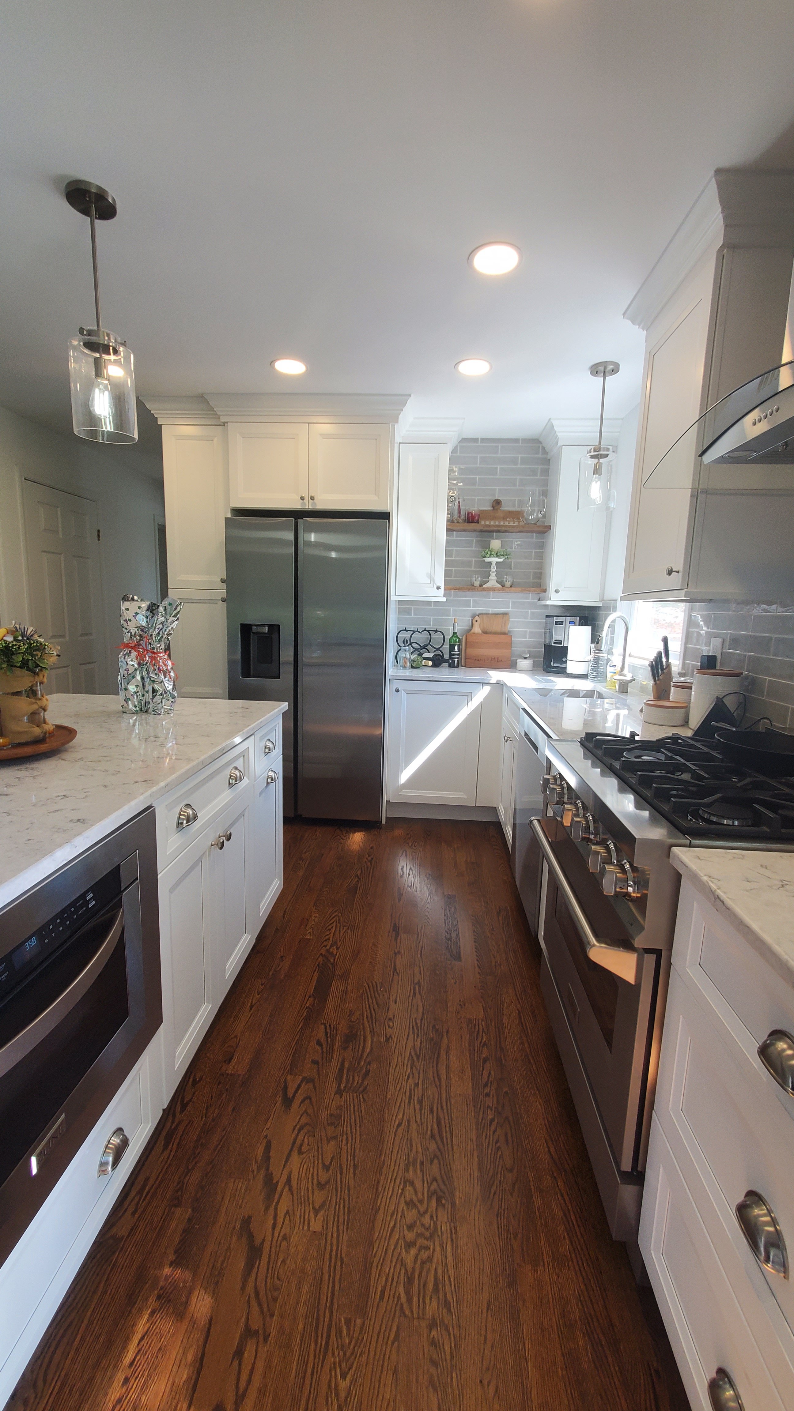 Gray plank tile flooring transitions to dark hardwood near a stainless steel range and hood, with white cabinetry and a marble-look countertop edging a dark wood island.