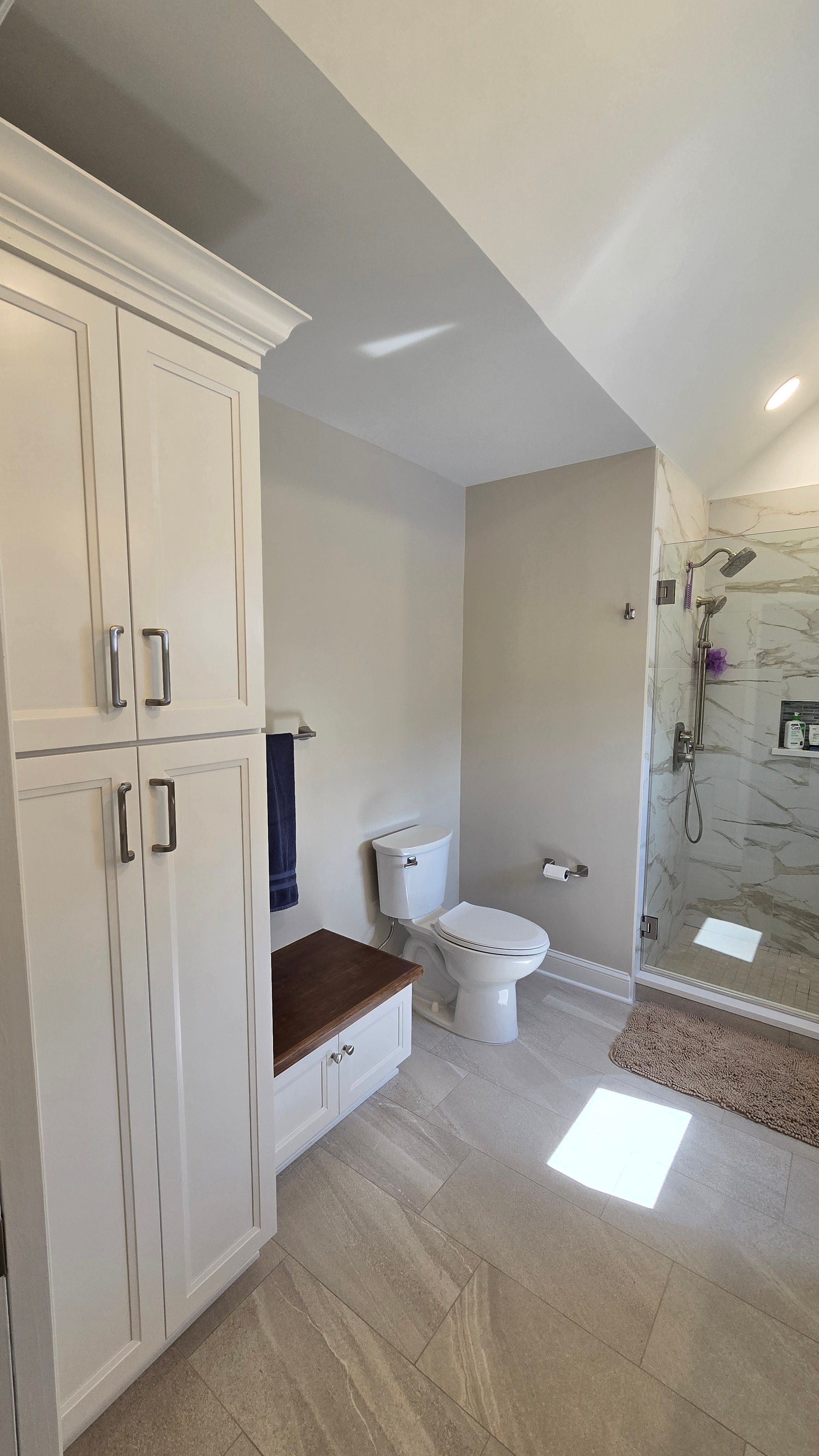 A toilet sits next to a white cabinet with a dark wood-toned counter edge and a navy towel on a wall bar.