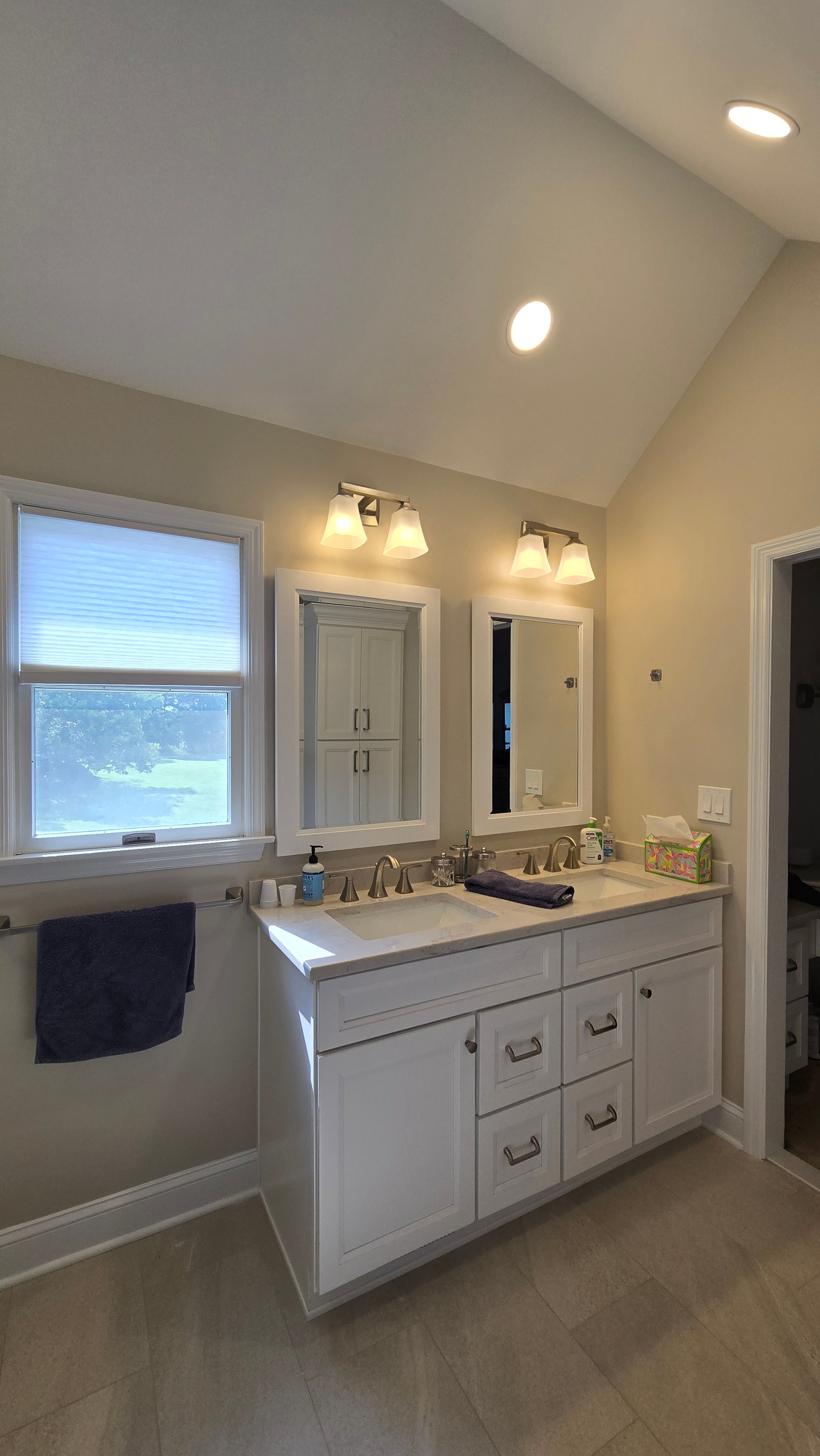A long vanity countertop has two separate framed mirrors, each flanked by a two-light brushed nickel sconce fixture.