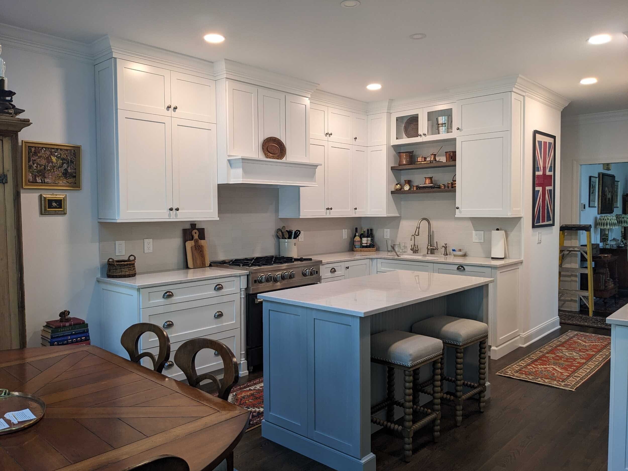 White shaker cabinets pair with a blue-painted island topped in white quartz, plus a stainless steel gas range under a shaped vent hood.