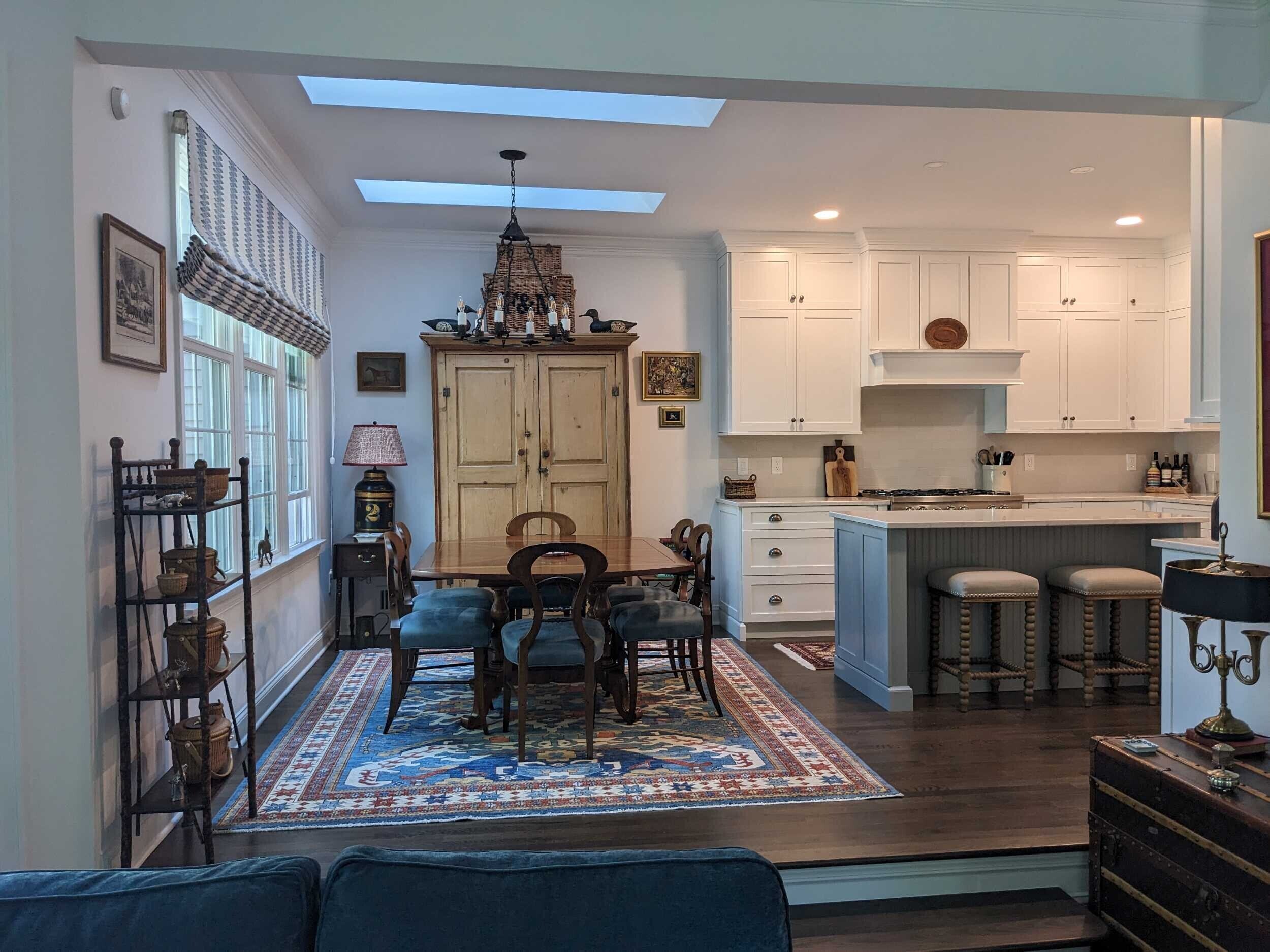 An open dining area with skylights adjoins a white kitchen featuring a blue island and stainless steel gas range.