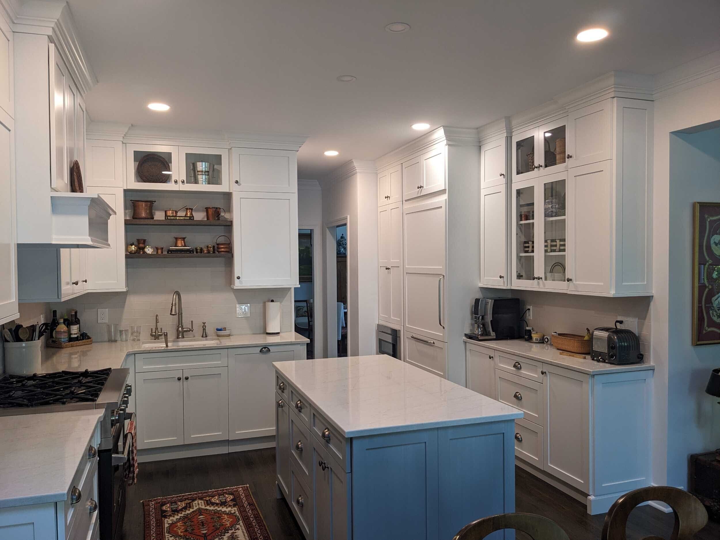 White shaker cabinets frame a paneled built-in refrigerator and glass-front uppers displaying copper cookware, mugs, and glassware.