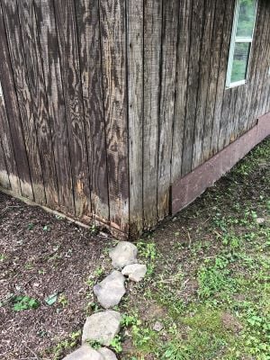 Before photo showing severely rotted and weathered wood siding at the base of a shed, with visible decay and gaps near the ground.