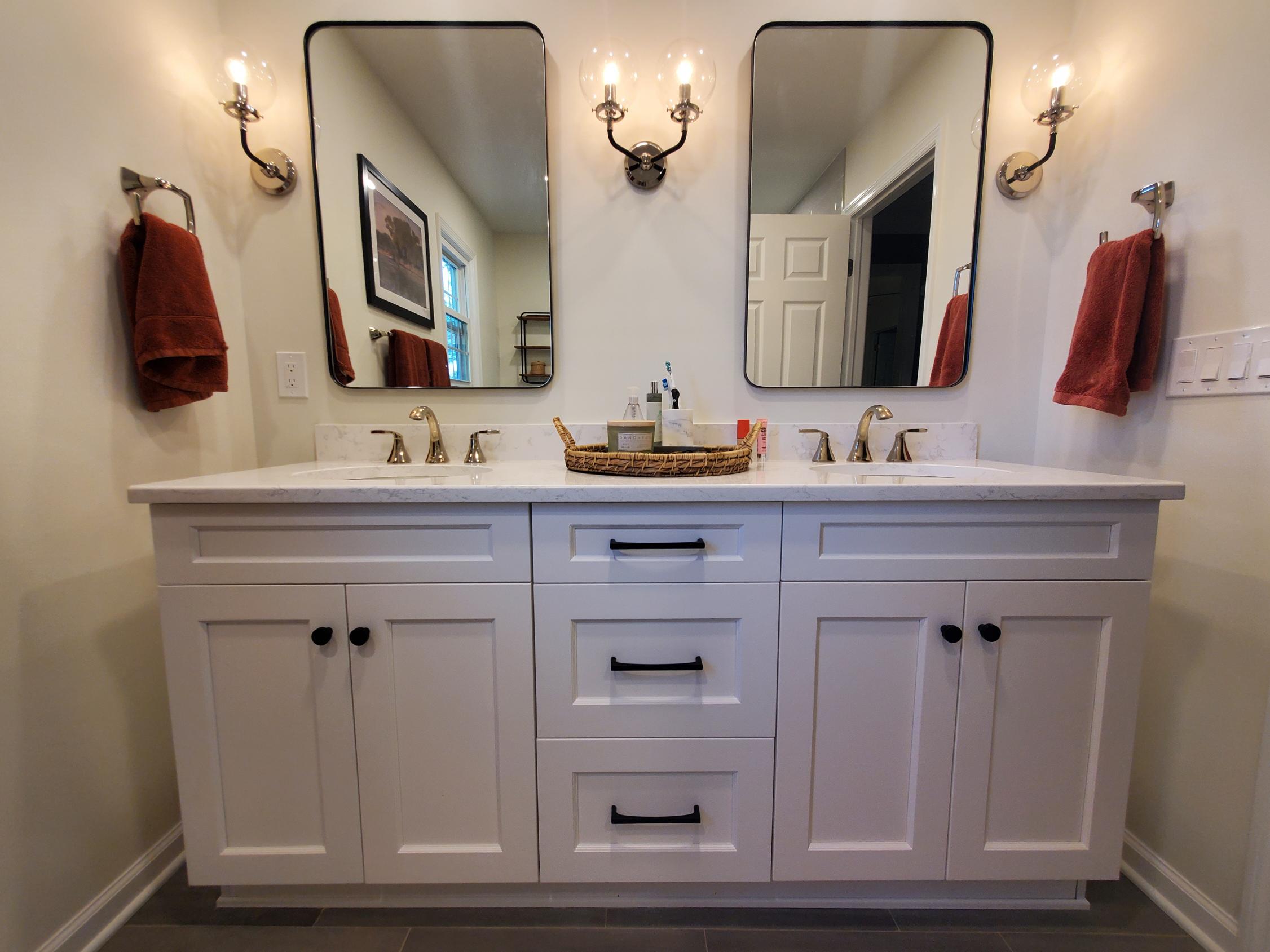 Double vanity bathroom with wall sconces and decorative mirrors