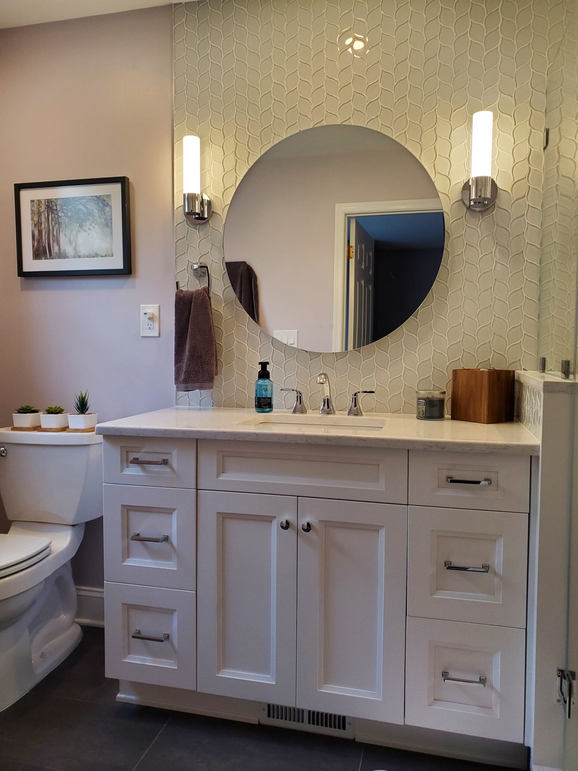 White vanity with circular mirror and wall sconces in remodeled bathroom